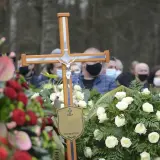 Drewniany krzyż z figurą Chrystusa na pogrzebie. Wieniec białych róż i czerwonych kwiatów. Ludzie w maseczkach. Co zrobić z krzyżem po pogrzebie?
