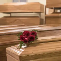 Wiele rodzajów trumien, niektóre ułożone piętrowo. Na jednej z nich bukiet czerwonych róż i złota obręcz.