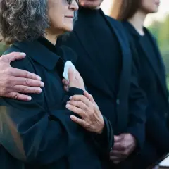 Odprawa pośmiertna: bliscy w żałobie, objęci ramieniem, trzymają chusteczkę.