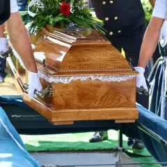 Pogrzebowa drewniana trumna z kwiatami, niesiona przez ludzi w białych rękawiczkach. Kto nie dostanie zasiłku pogrzebowego?