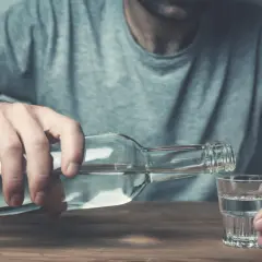 Mężczyzna nalewa alkohol do kieliszka. To może być jeden z objawów przed śmiercią alkoholika, symbol jego walki.