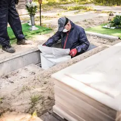 Pracownik w masce i rękawiczkach wyciąga worek z grobu. Obok trumna. Cena ekshumacji po 30 latach.