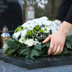 Dłonie układają wieniec na nagrobku. Czas żałoby w Kościele katolickim jest czasem refleksji i pamięci.