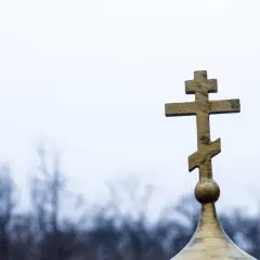 Złoty krzyż prawosławny na tle pochmurnego nieba. Symbolizuje nadzieję i pamięć podczas pogrzebu prawosławnego.
