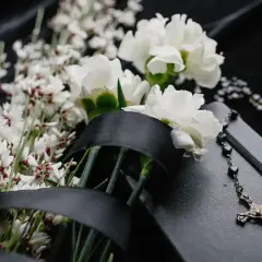 Białe kwiaty, czarna wstęga i różaniec na czarnej okładce. Symboliczny gest pamięci, kto niesie zdjęcie na pogrzebie.
