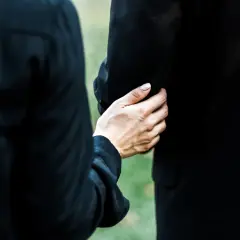 Dłoń obejmuje ramię, wspierając w trudnym momencie. To obraz żałoby i wspólnego przeżywania straty podczas orszaku pogrzebowego.