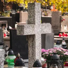 Kamienny krzyż i znicze na cmentarzu. W tle nagrobki i jesienne liście. Warto zadbać o porządek, by wiedzieć, jak usunąć chwasty na cmentarzu.