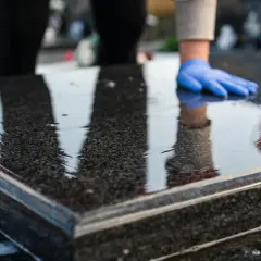 Ręce w niebieskich rękawiczkach czyszczą mokry granit. Dowiedz się, czym myć pomnik z granitu, by wyglądał jak nowy.