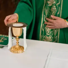 Kapłan w zielonej szacie przygotowuje kielich podczas mszy żałobnej.
