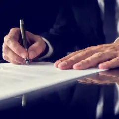 Mężczyzna w garniturze podpisuje dokument. Warto wiedzieć, ile kosztuje akt zgonu, aby móc dopełnić formalności.