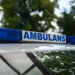 Napis "AMBULANS" na niebieskim świetle. Służby przyjechały na miejsce, gdzie doszło do zgonu w domu. Policja zabezpiecza teren.