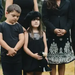 Dzieci w czarnych ubraniach, chłopiec w koszulce, dziewczynka w sukience z beretem, trzymająca pluszaka. Wskazówka, jak ubrać dziecko na pogrzeb.