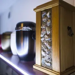 Drewniana urna z kamieniami i piaskiem, obok inne urny. Symbol pamięci po kremacji.
