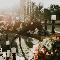 Stół z bogatą dekoracją kwiatową i świecami, tworzący atmosferę uroczystości. Może to być ceremonia pogrzebowa inaczej, pełna zadumy i piękna.