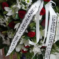 Wieniec z białych lilii i czerwonych róż z katolickim napisem na szarfie pogrzebowej: "Z ostatnim pożegnaniem".