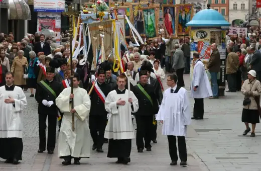 Procesja religijna z chorągwiami i duchownymi w strojach. Długość mszy świętej może być różna, ale ta uroczystość trwa.