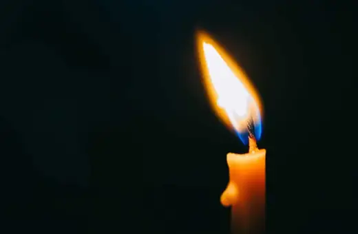 Płonąca świeca w ciemności, symbol tęsknoty za zmarłą osobą. Cytaty o stracie i pamięci.