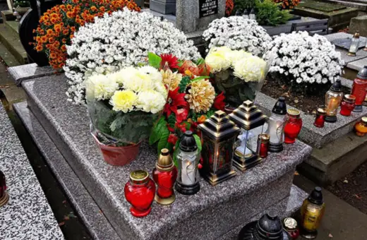 Kwiaty i znicze na grobie. Jak ozdobić pomnik tymczasowy? Bukiet chryzantem i czerwone róże dodają koloru.