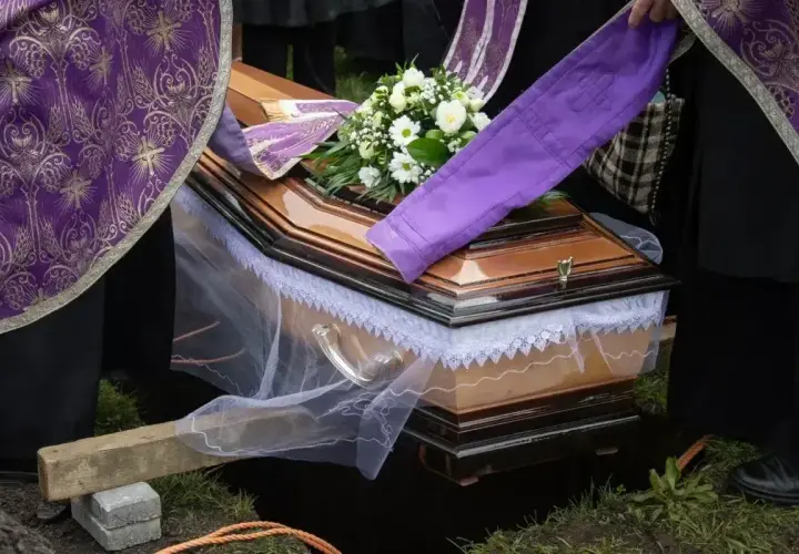 Uroczyste chowanie zmarłego po niedzieli. Trumna z kwiatami, otoczona przez żałobników w strojach liturgicznych, opuszczana do grobu.