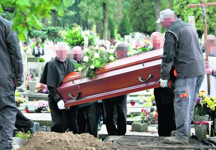 Pogrzeb na cmentarzu. Kilku mężczyzn niesie drewnianą trumnę ozdobioną kwiatami w kierunku grobu głębinowego.