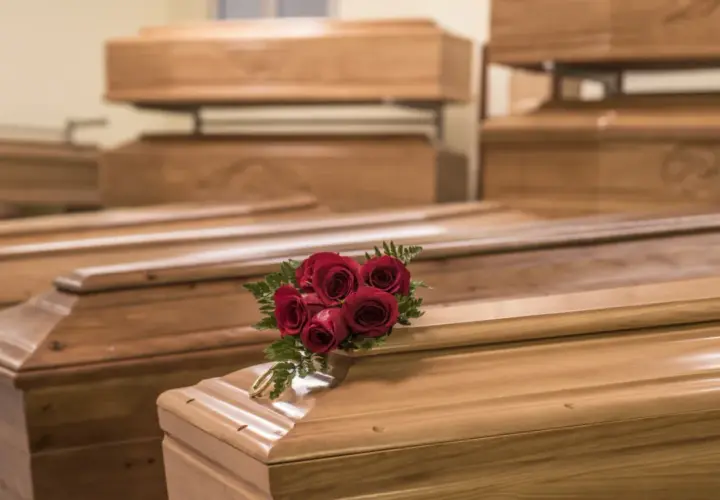 Wiele rodzajów trumien, niektóre ułożone piętrowo. Na jednej z nich bukiet czerwonych róż i złota obręcz.