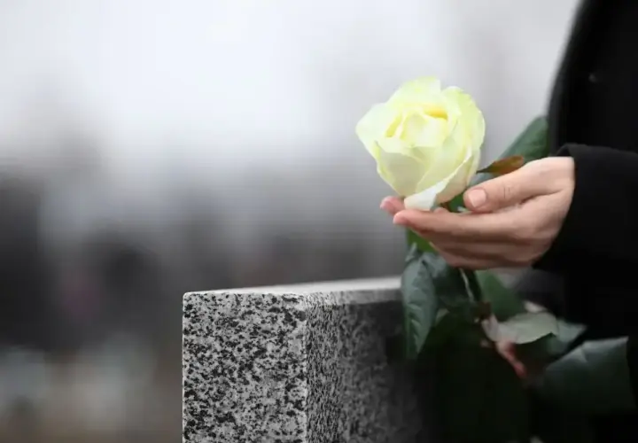 Dłoń trzyma białą różę przy nagrobku. Pytanie, jak długo nie można ruszać rzeczy zmarłego, pozostaje otwarte.