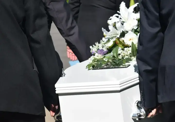 Biała trumna z kwiatami niesiona przez żałobników. Zastanawiasz się, ile kosztuje trumna?