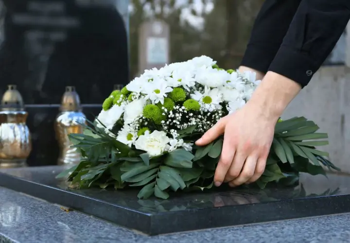 Dłonie układają wieniec na nagrobku. Czas żałoby w Kościele katolickim jest czasem refleksji i pamięci.