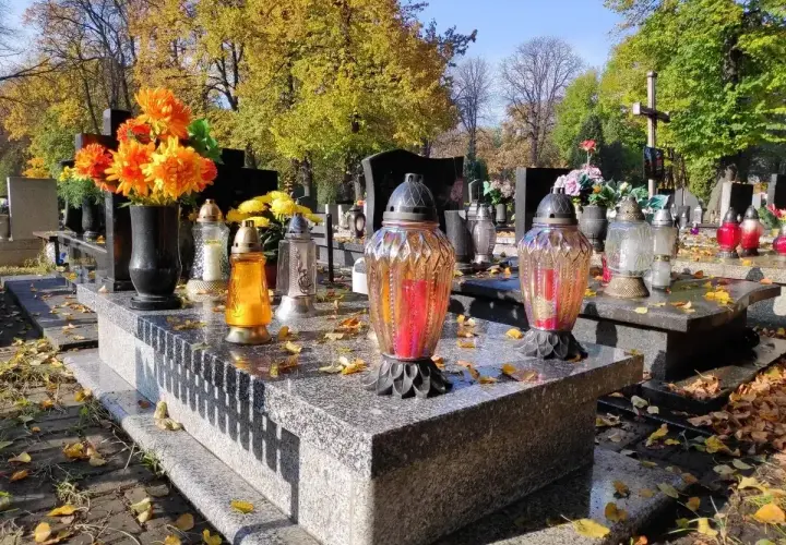 Jesienny dzień na cmentarzu. Na kamiennym, murowanym grobie palą się znicze, a obok stoją świeże kwiaty.