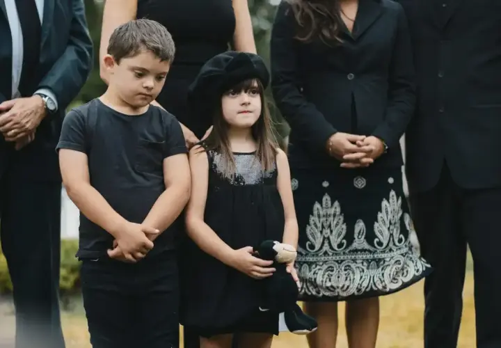 Dzieci w czarnych ubraniach, chłopiec w koszulce, dziewczynka w sukience z beretem, trzymająca pluszaka. Wskazówka, jak ubrać dziecko na pogrzeb.