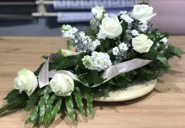 Białe róże na drewnianym stole, ozdobione wstęgą. Biała róża symbolizuje czystość i niewinność, często wybierana na uroczystości.