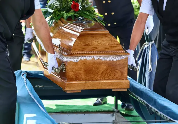 Smutny pogrzeb dziecka. Drewniana trumna z kwiatami niesiona do grobu przez żałobników w białych rękawiczkach.