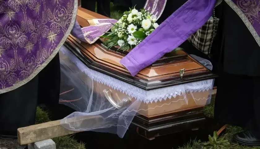 Uroczyste chowanie zmarłego po niedzieli. Trumna z kwiatami, otoczona przez żałobników w strojach liturgicznych, opuszczana do grobu.