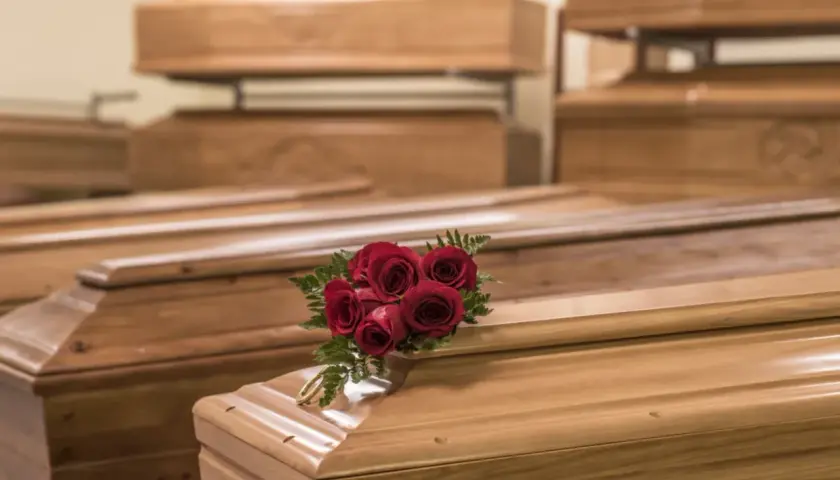 Wiele rodzajów trumien, niektóre ułożone piętrowo. Na jednej z nich bukiet czerwonych róż i złota obręcz.