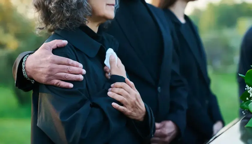 Odprawa pośmiertna: bliscy w żałobie, objęci ramieniem, trzymają chusteczkę.