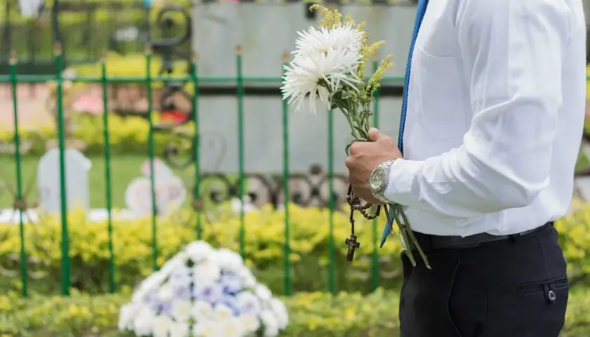 Mężczyzna w białej koszuli i niebieskim krawacie trzyma bukiet białych kwiatów i różaniec. To jego urlop okolicznościowy śmierć szwagra.