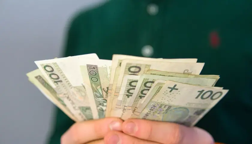 Dłonie trzymają wachlarz banknotów 100 zł. To może być pomocne przy pytaniu, co to jest renta rodzinna.