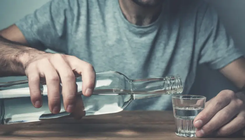Mężczyzna nalewa alkohol do kieliszka. To może być jeden z objawów przed śmiercią alkoholika, symbol jego walki.