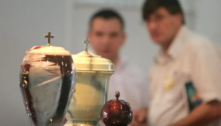 Trzy urny pogrzebowe z krzyżami, w tle niewyraźne postacie. Temat kremacji budzi dyskusje, nawet wśród hierarchów Kościoła, jak papież o kremacji.