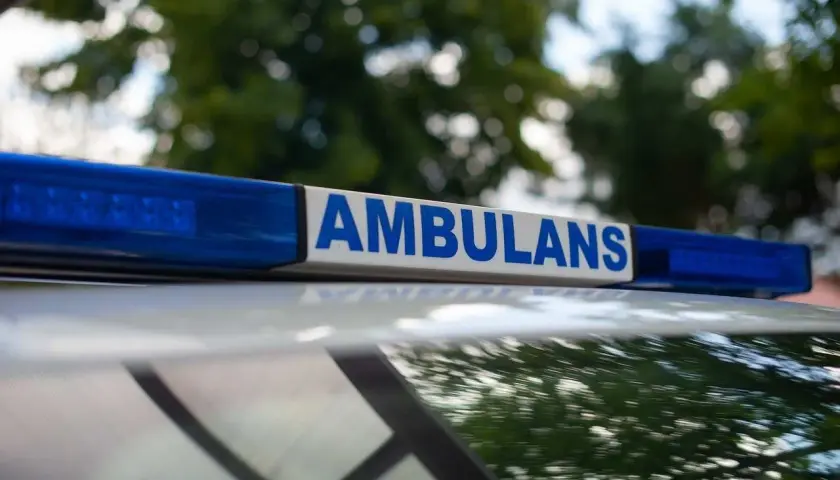 Napis "AMBULANS" na niebieskim świetle. Służby przyjechały na miejsce, gdzie doszło do zgonu w domu. Policja zabezpiecza teren.