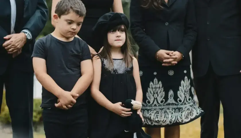 Dzieci w czarnych ubraniach, chłopiec w koszulce, dziewczynka w sukience z beretem, trzymająca pluszaka. Wskazówka, jak ubrać dziecko na pogrzeb.