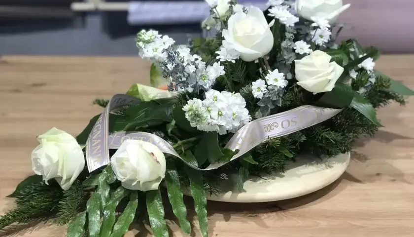 Białe róże na drewnianym stole, ozdobione wstęgą. Biała róża symbolizuje czystość i niewinność, często wybierana na uroczystości.