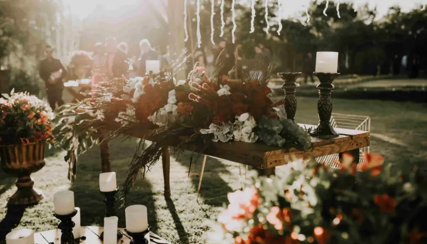 Stół z bogatą dekoracją kwiatową i świecami, tworzący atmosferę uroczystości. Może to być ceremonia pogrzebowa inaczej, pełna zadumy i piękna.