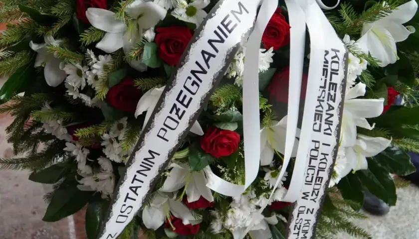 Wieniec z białych lilii i czerwonych róż z katolickim napisem na szarfie pogrzebowej: "Z ostatnim pożegnaniem".