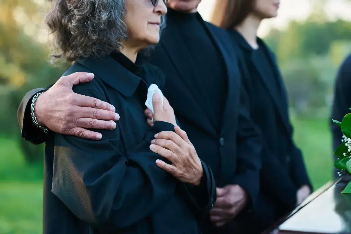 Odprawa pośmiertna: bliscy w żałobie, objęci ramieniem, trzymają chusteczkę.