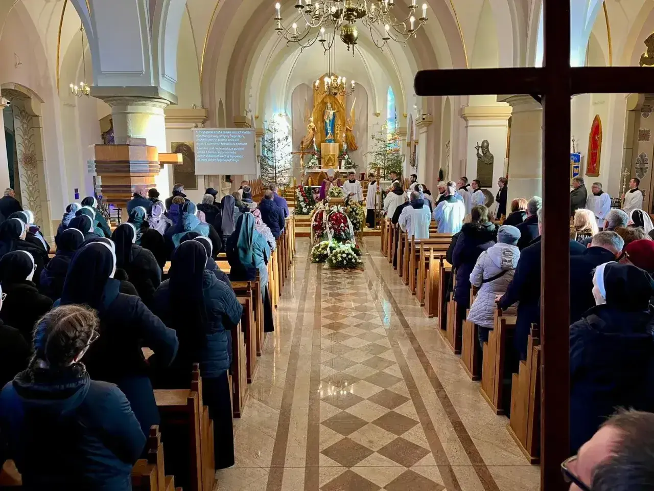 Uroczystość pogrzebowa w kościele. Wierni, w tym siostry zakonne, słuchają współczesnych pieśni pogrzebowych.