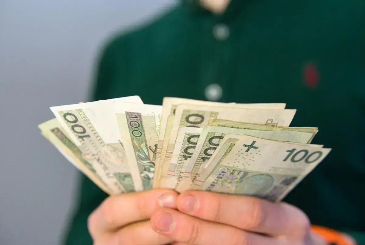 Dłonie trzymają wachlarz banknotów 100 zł. To może być pomocne przy pytaniu, co to jest renta rodzinna.