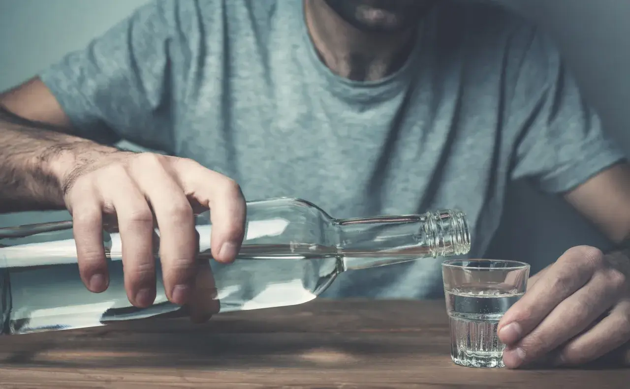 Mężczyzna nalewa alkohol do kieliszka. To może być jeden z objawów przed śmiercią alkoholika, symbol jego walki.