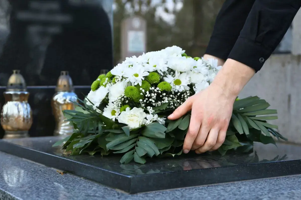 Dłonie układają wieniec na nagrobku. Czas żałoby w Kościele katolickim jest czasem refleksji i pamięci.