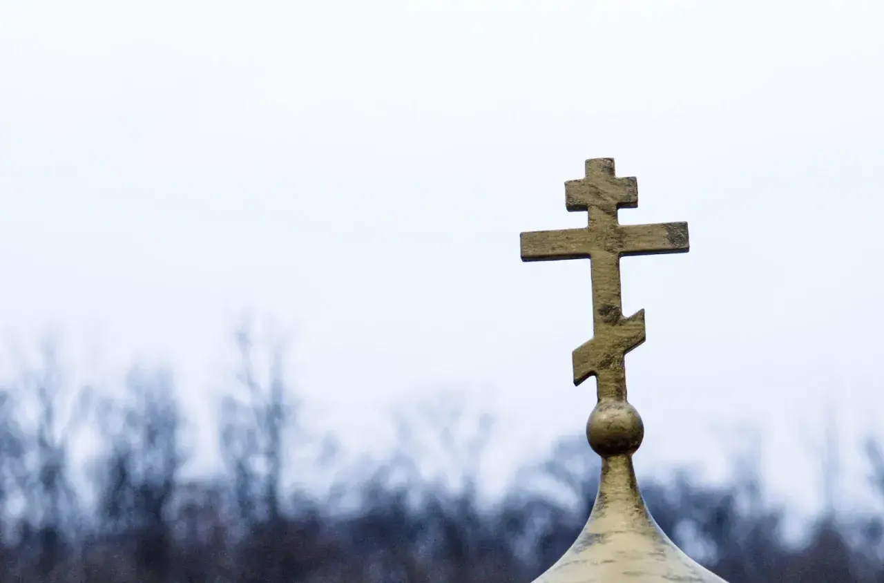 Złoty krzyż prawosławny na tle pochmurnego nieba. Symbolizuje nadzieję i pamięć podczas pogrzebu prawosławnego.